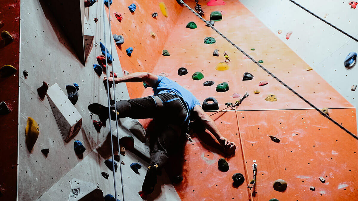 Mann, der gesichert eine Boulderwand in der Kletterhalle Cityrock am Berliner Platz (Hohe Straße) hochklettert